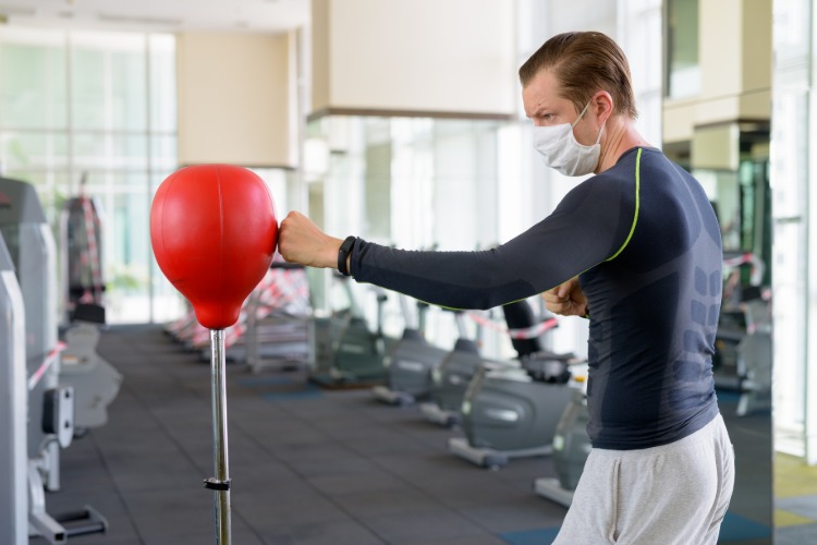 mann mit schutzmaske übt körperliche aktivität durch training im fitnessstudio bei coronavirus