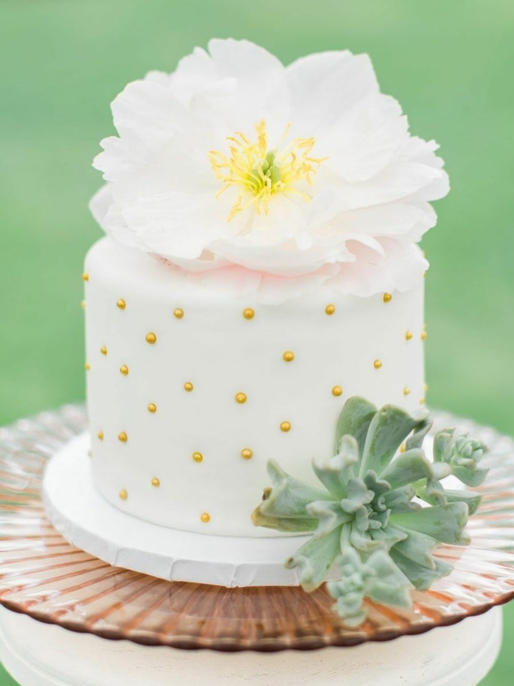 Weiße Hochzeitstorte mit goldenen Perlen verziert und großer Blume und Sukkulente