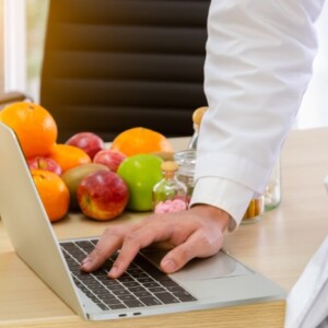 ernährungsexperte recherchiert am laptop in seinem büro mit gesunden obst und gemüse im hintergrund