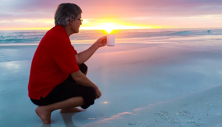 mann mit tasse in der hand tankt vitamin d aus dem sonnenuntergang am strand