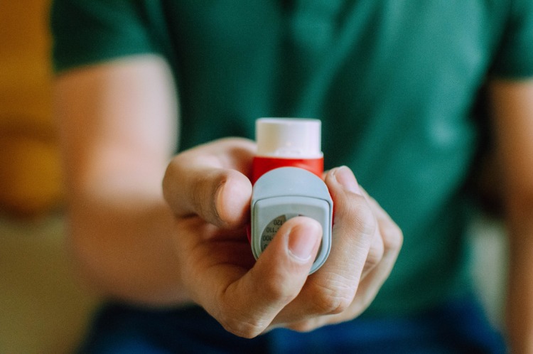 mann hält einen inhalator mit medikament gegen asthma während der covid 19 pandemie