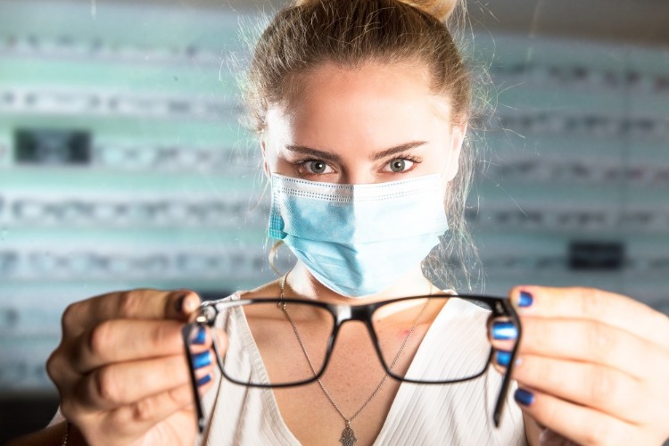 verkäuferin in einer optik bietet dem kunden korrekturbrille während covid 19 pandemie an