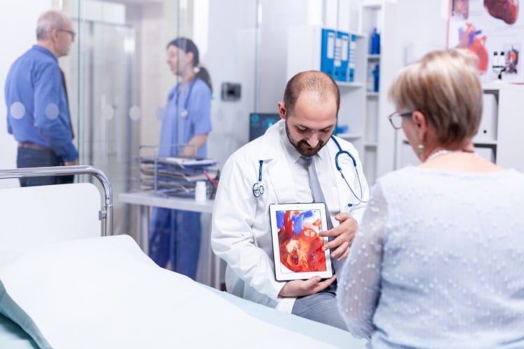 arzt zeigt seiner patientin details über ihre herzerkrankung auf einem tablett im krankenhaus