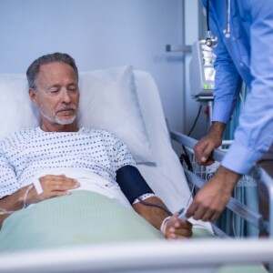 älterer mann im krankenbett wird vom arzt auf blutdruck nach herzinfarkt untersucht