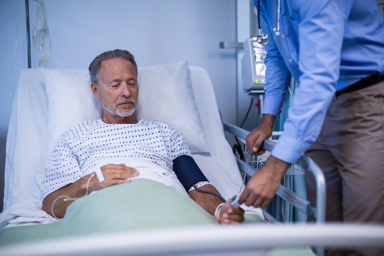 älterer mann im krankenbett wird vom arzt auf blutdruck nach herzinfarkt untersucht