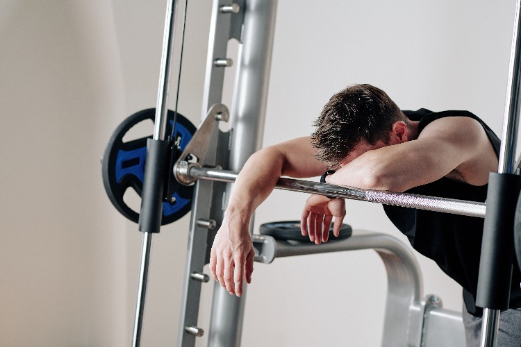 druch extreme fitness erschöpfter mann lehnt sich an gewichten im fitnessstudie