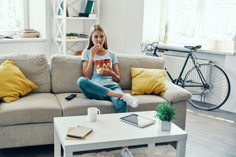junge Frau isst Popcorn auf dem Sofa im Wohnzimmer