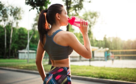 junge frau trinkt sportgetränk aus plastikflasche beim training