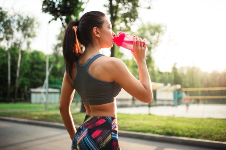 junge frau trinkt sportgetränk aus plastikflasche beim training