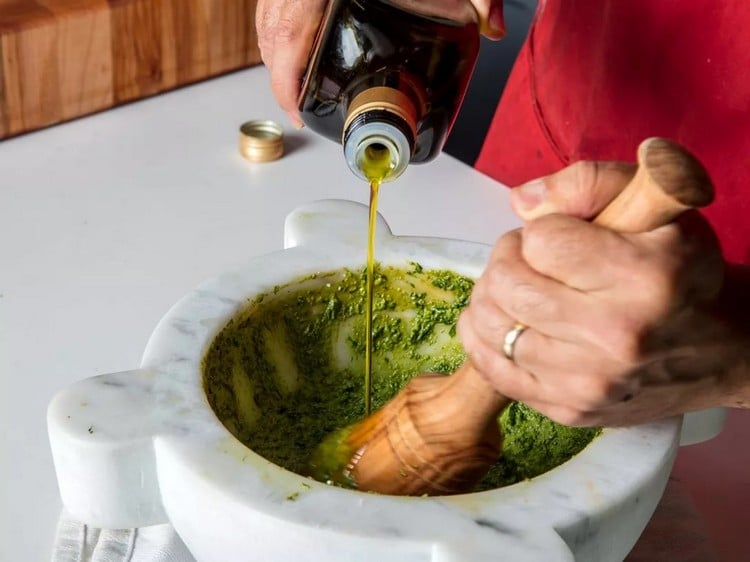 Olivenöl in Mörser zu Basilikum hinzufügen