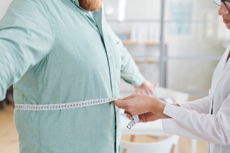 ärztin misst bauchumfang vom patienten wegen den auswirkungen von übergewicht auf covid 19