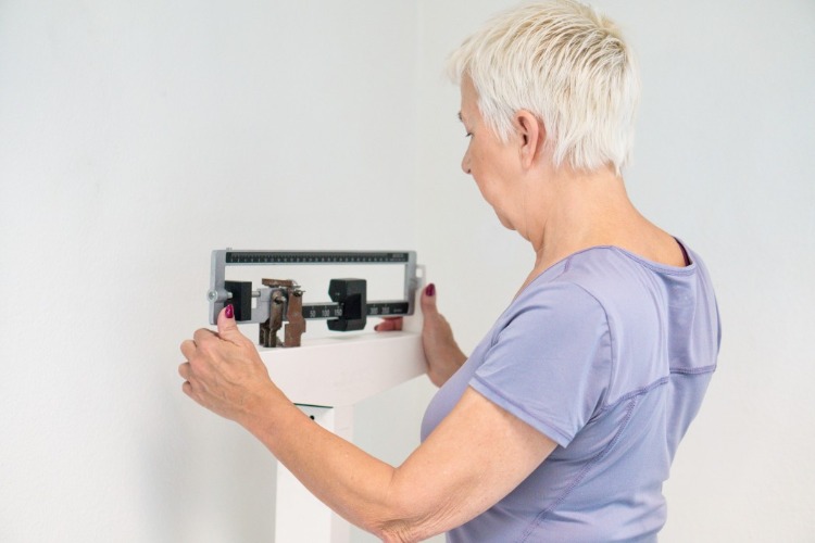 Een vrouw op een weegschaal controleert op oudere leeftijd het calorieverbruik en de stofwisseling