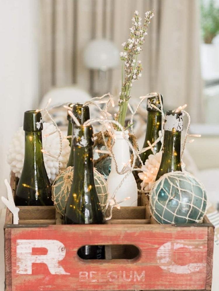 Idee für eine Weinkiste mit Fächern - Glasflaschen, Lichterketten und Blumen als Dekoration