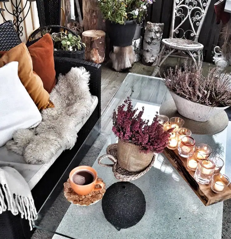 herbstdeko auf terrasse mit teelichtern, heidekraut und warmen stoffen