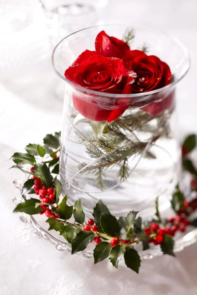 Rote Rosen und Tannenzweige im Glas mit Mini-Kranz aus Stechpalmen als Akzent