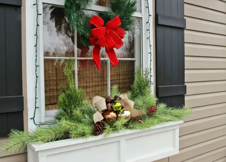 Weihnachtsdeko im Blumenkasten am Fenster - Christbaumkugeln und Zapfen in einer Schleife