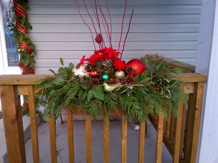 Weihnachtsdeko im Blumenkasten am Geländer der Veranda mit roten Akzenten