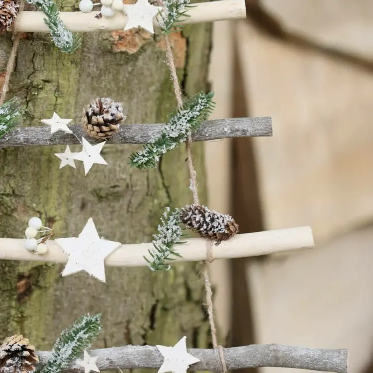 Leiter weihnachtlich schmücken mit Sternen und Naturmaterialien und an einen Baum lehnen