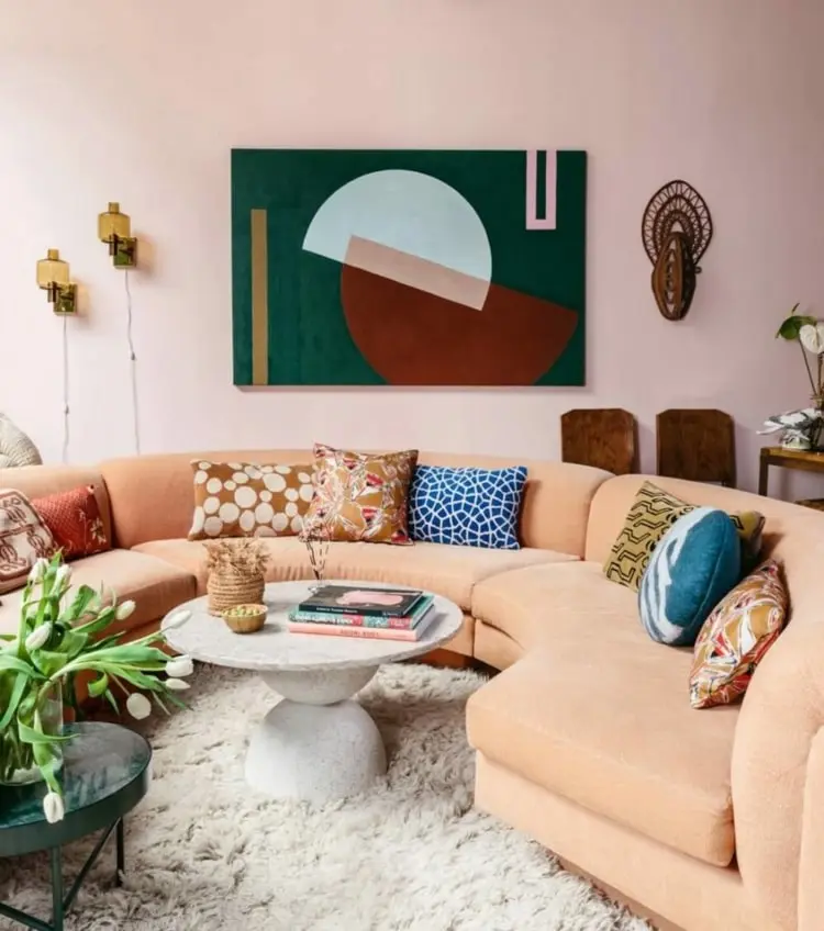 Cremefarbene runde Couch im Wohnzimmer mit abstraktem Wandbild und rundem Couchtisch in Beton-Optik