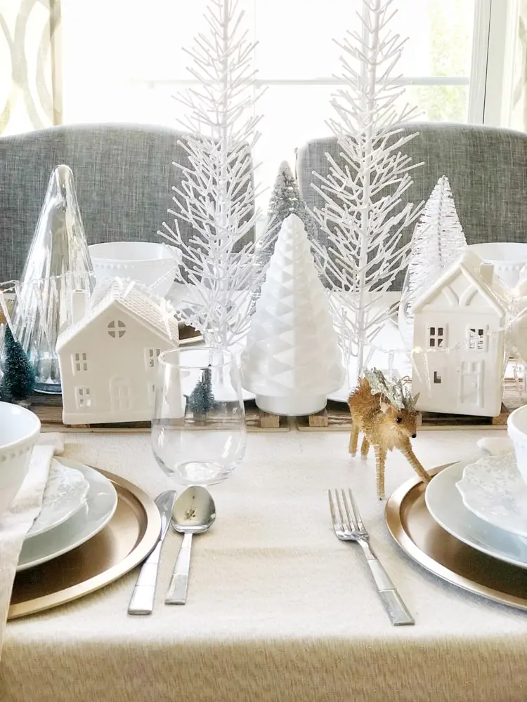 Kleine, weiße Häuser und Bäume für die Tischmitte als Winterdeko auf dem Tisch aufstellen