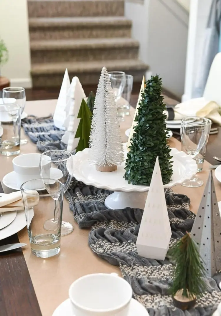 Künstliche Tannenbäume aus Kunststoff und Papier für einen Mini-Wald auf grauem Tischläufer