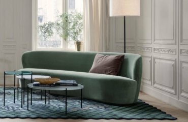 Runde Couch im Wohnzimmer in dezentem Grün mit abstrakt gemustertem Teppich