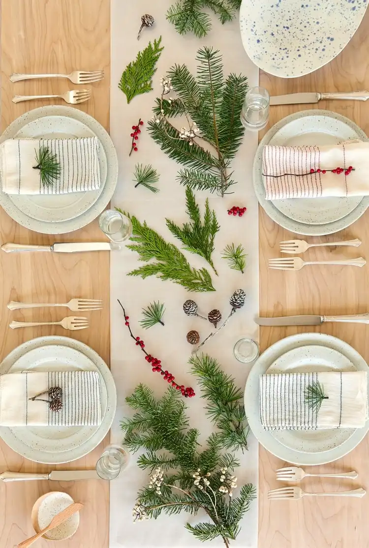 Winterdeko selbstgemacht - Immergrüne Zweige und Beeren auf einem Tischläufer verteilen
