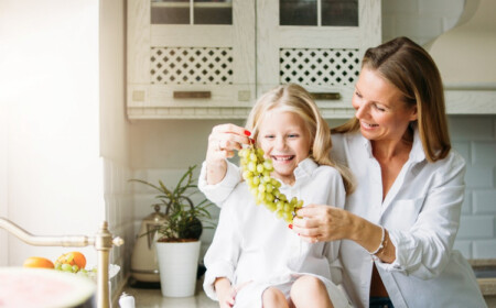 kleines mädchen und mutter halten weiße trabenfrucht und lachen in der küche