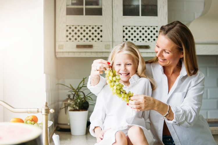 kleines mädchen und mutter halten weiße trabenfrucht und lachen in der küche