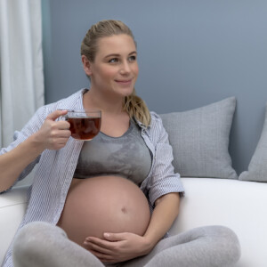lächelnde schwangere frau mit babybauch hält einen tee