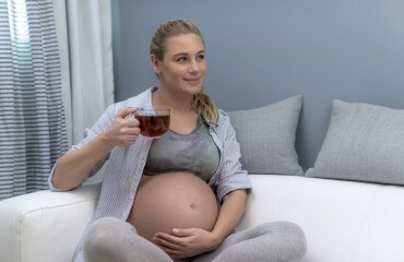 lächelnde schwangere frau mit babybauch hält einen tee