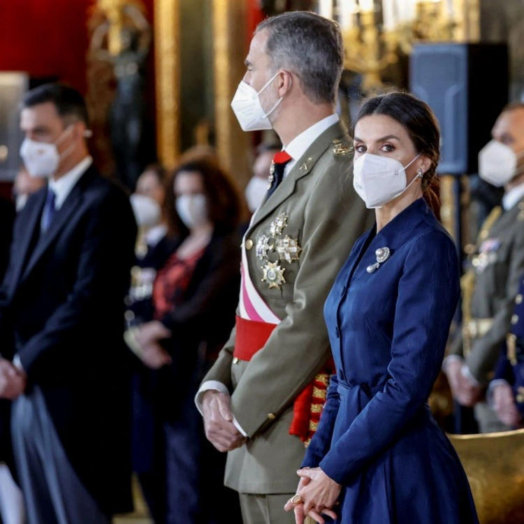 Reyes españoles en un acto militar con máscaras protectoras y elegantes disfraces