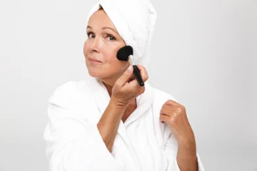 Ältere frau, die sich rouge auf die wangen aufträgt