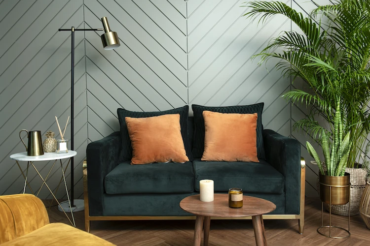 naturnaher wohnraum im retro stil und smaragdgrüne couch mit orangenfarbenen kissen