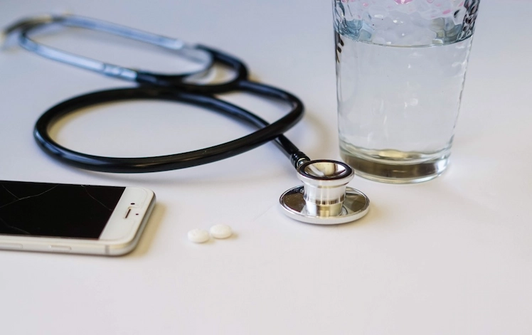 stethoskop und handy neben glas mit wasser und medikamenten