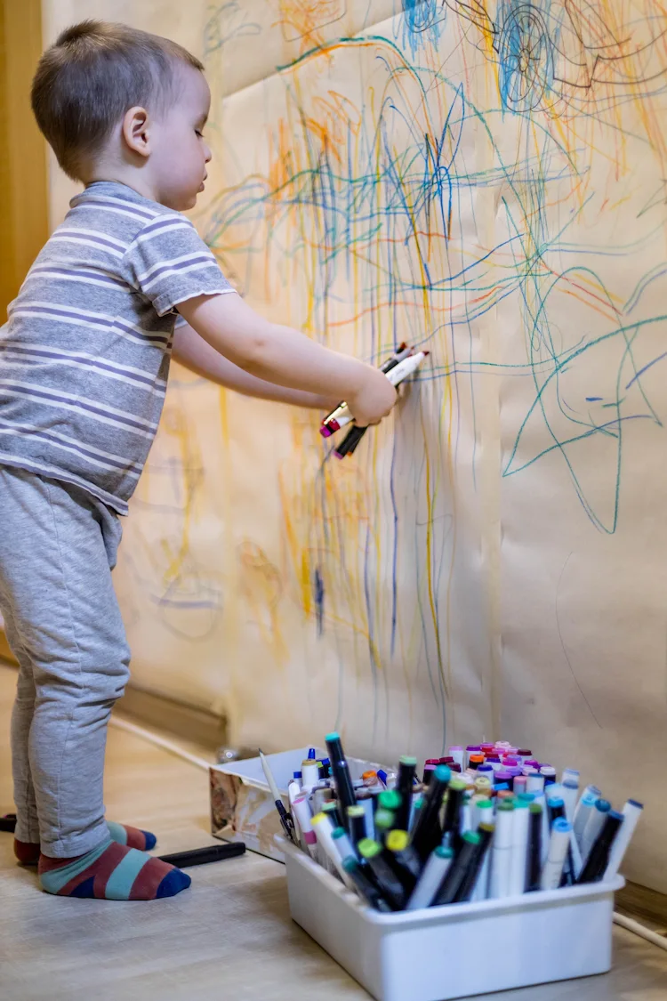 kleiner junge zeichnet auf den wänden im eigenen zuhause mit wachsmalstiften