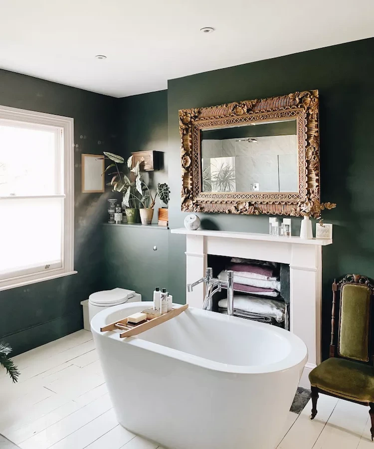 dark green walls and antique mirror in the bathroom with white bathtub