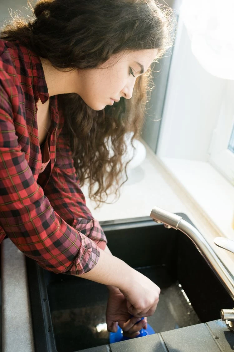 junge Frau entpumpt verstopftes Küchenabflussrohr weil Abfluss stinkt