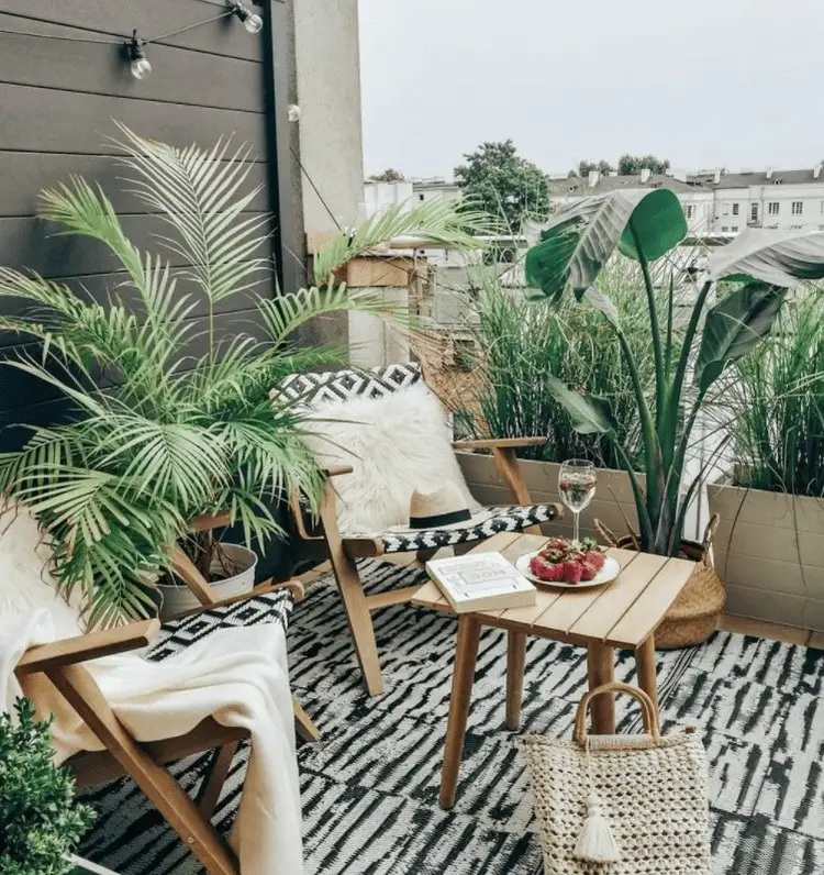 Eleganter, sommerlicher Balkon in Schwarz und Weiß, dekoriert mit vielen Pflanzen und Holzmöbeln
