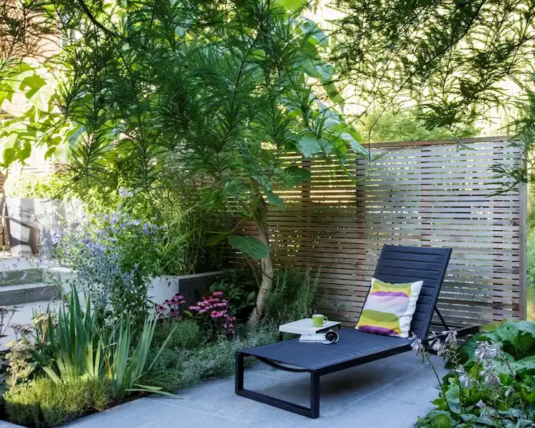 gemütlicher patio bereich mit liege und umgebenden pflanzen neben schattenspendendem baum