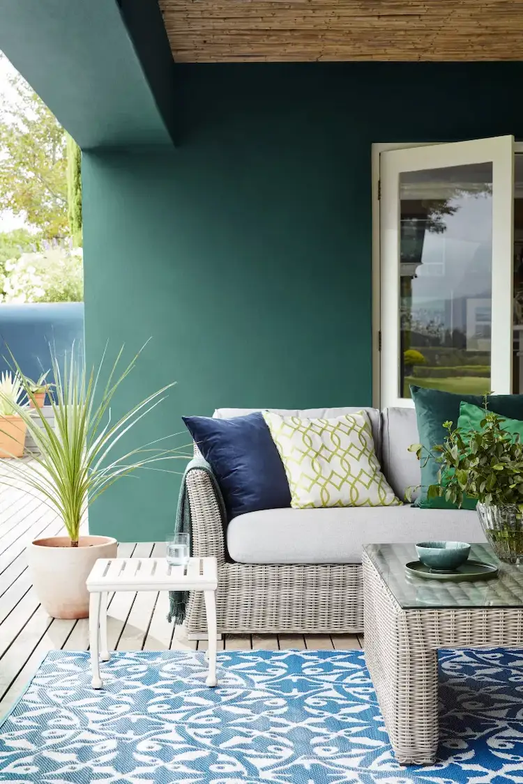in grün gefärbte außenwand als kulisse für farbenfrohe terrassengestaltung mit pflanzen