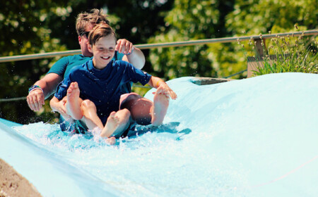 kleiner junge und sein vater haben spaß im sommer auf einer wasserrutsche