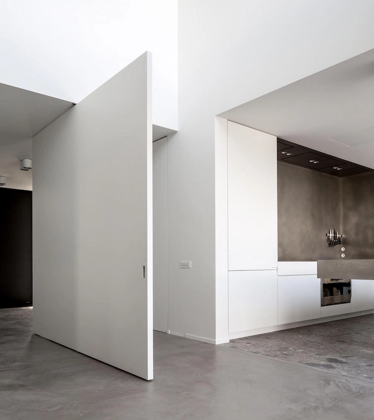minimalistischer wohnraum mit überdimensionaler tür in weiß und grauem boden
