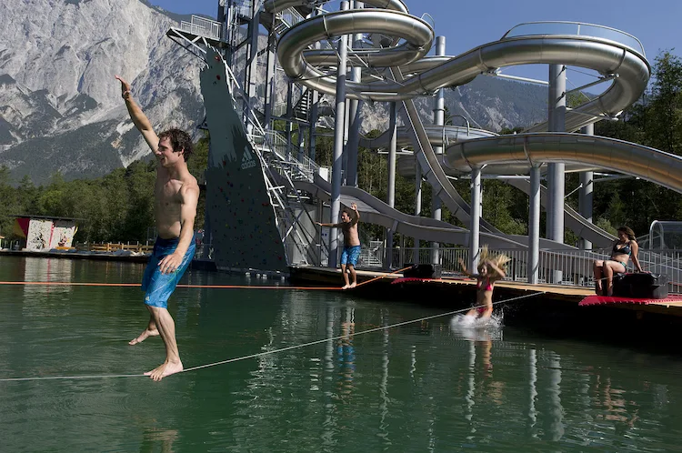 junger mann im aquapark area 47 balanciert auf einem seil über dem see neben großer wasserrutsche