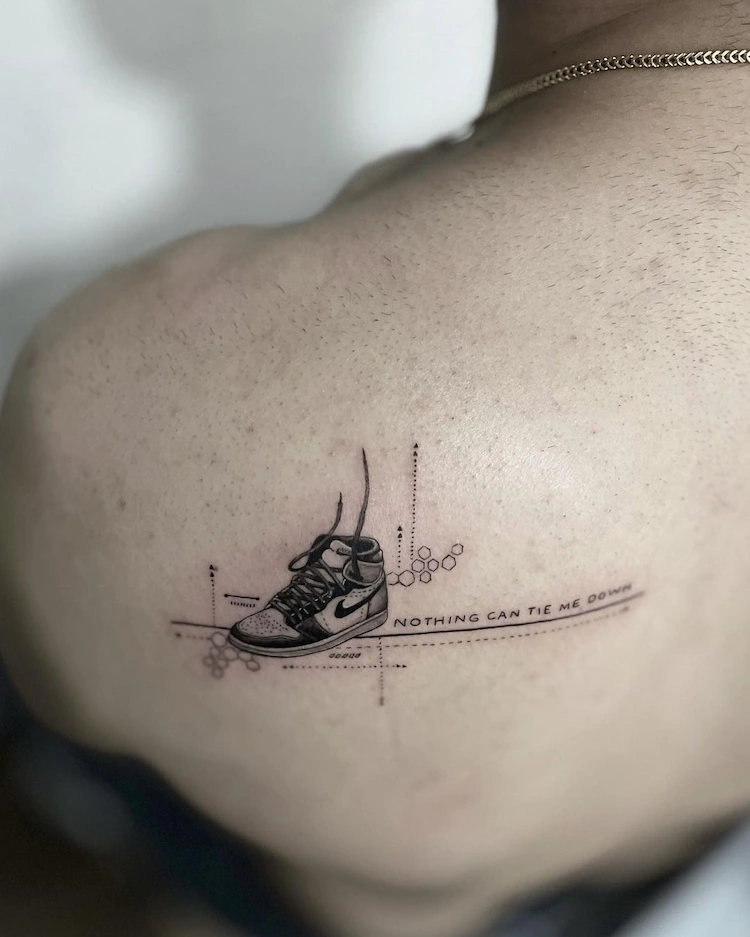 schulter tattoo im mikrorealistischen stil mit turnschuh und kleiner schrift als motto neben details