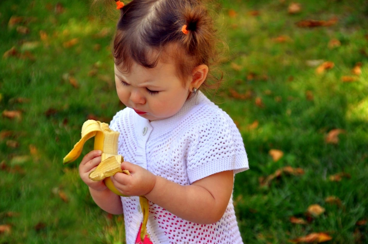 kleines mädchen im garten isst eine banane