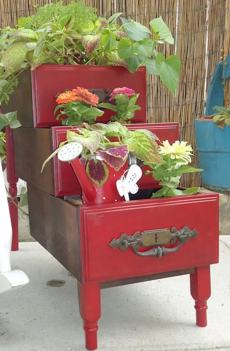 drei aufeinander gestapelte schreibtischschubladen in roter farbe mit passender bepflanzung als dekoration