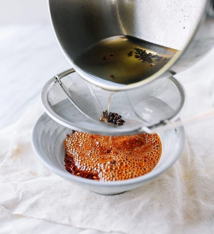 durchsieben von heißem paprikaöl in eine kleine keramikschüssel für die spätere aufbewahrung im kühlschrank