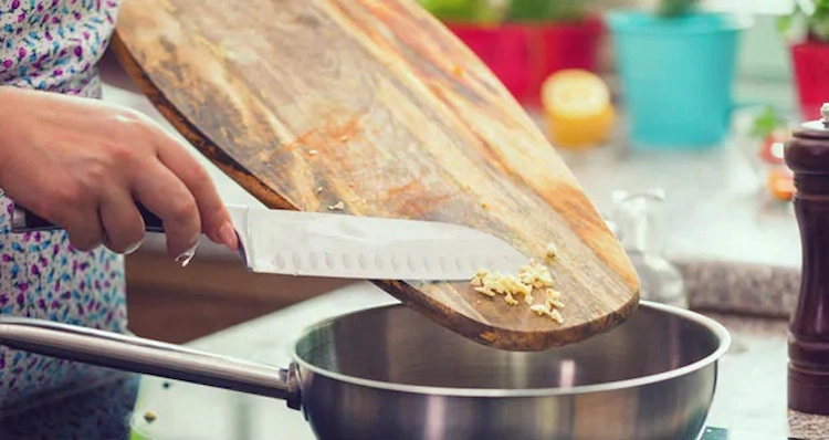 geschnittene knoblauchzehen aus einem küchenbrett ins gericht werfen und den geschmack verbessern