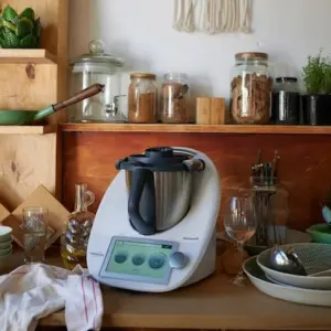 rustikal eingerichtete küche mit holzregalen und küchenutensilien um einer moderner küchenmaschine verteilt